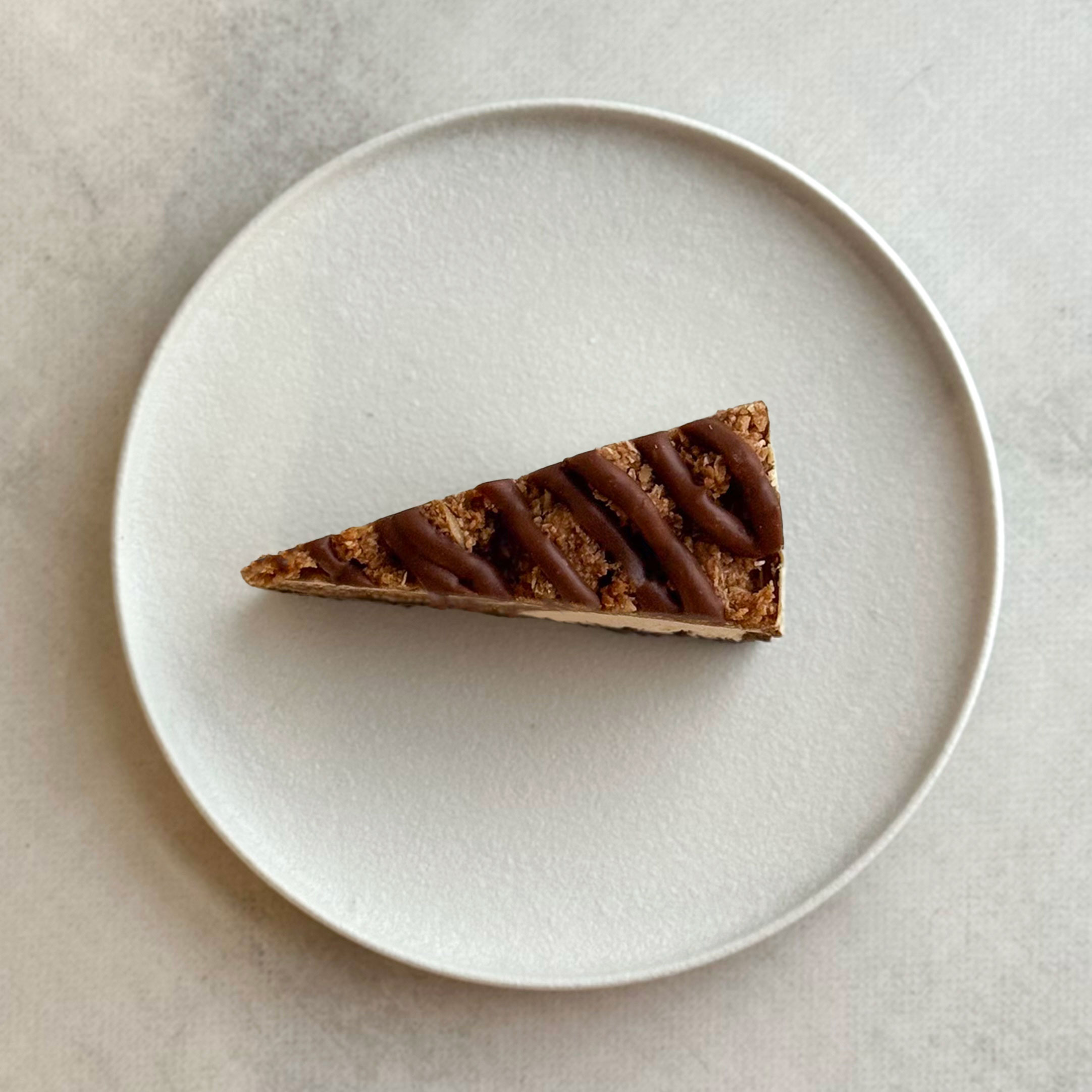 Нежный чизкейк из творожного сыра с начинкой из мягкого кокосового кранча с мякотью кокоса на песочно-шоколадной подложке. Сверху украшен кокосовым кранчем и залит карамелью. изображение 2