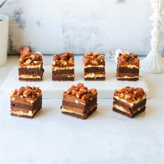 Сладко-соленые арахисовые орешки, светлый и молочный шоколад, сливочная карамель между двумя слоями брауни. Макушка украшена орешками.
